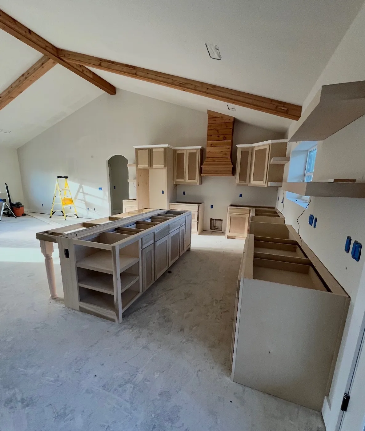Wide view of kitchen cabinetry during installation below exposed beams