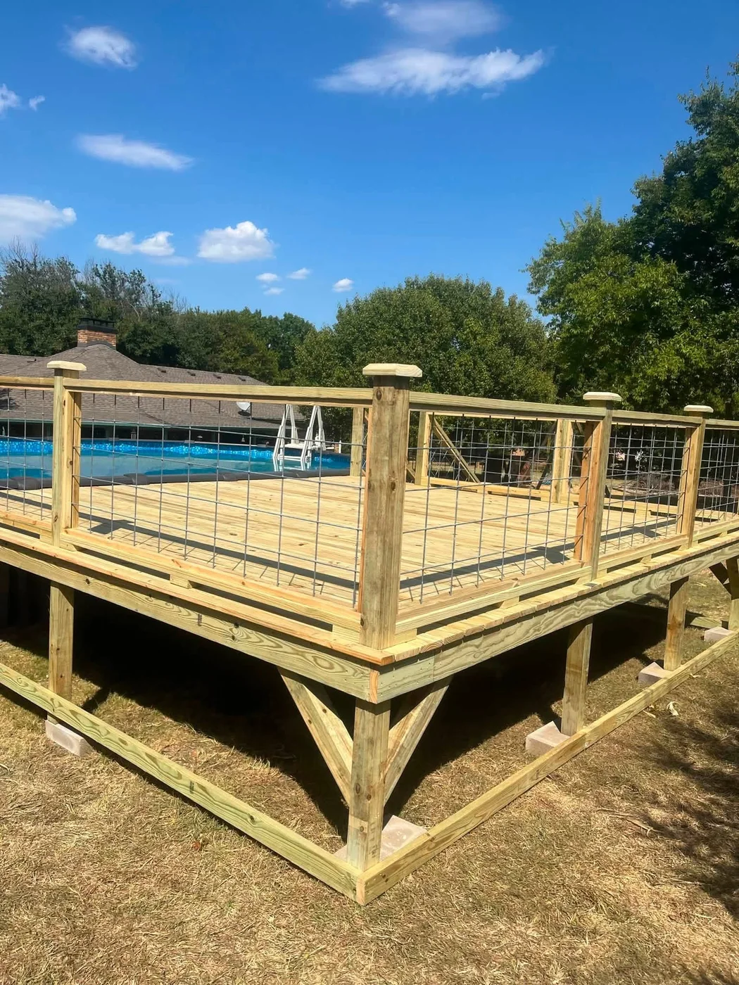 Raised wood pool deck with capped posts and wire-panel railing on a sunny day.